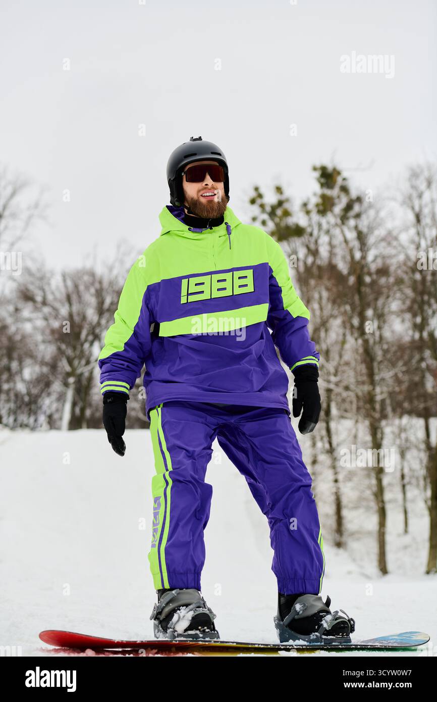 Un uomo con la barba ama lo snowboard su una pista innevata circondata da alberi invernali e clima fresco. Foto Stock