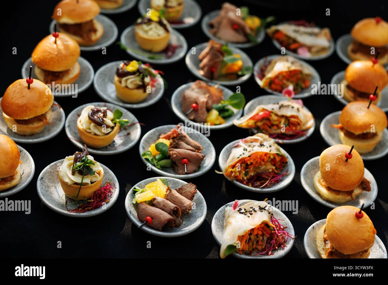 Vari mini bocconcini tra cui panini, fette di manzo, involtini di verdure e tartine disposti su piccoli piatti. Ideale per catering, eventi o ricevimenti. Foto Stock