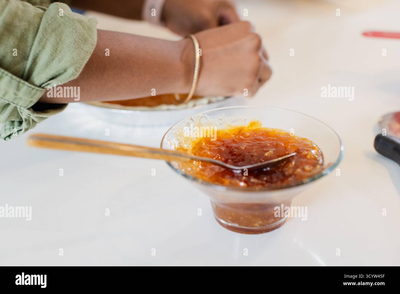 Recipiente di vetro trasparente con marmellata d'arancia, con cucchiaio di legno e teglia per torte Foto Stock