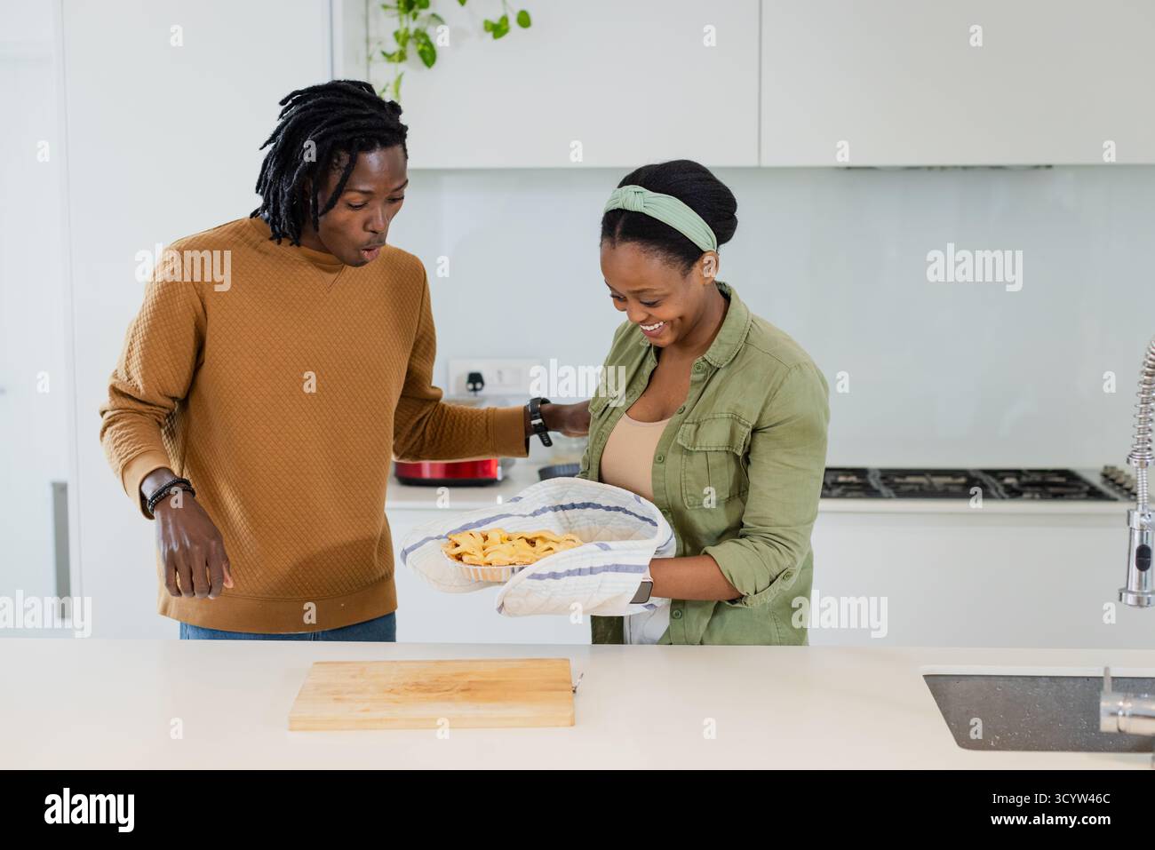 Una coppia afroamericana che cucina, tenendo le tortilla chips in piatto indossando il guanto da forno sull'isola della cucina Foto Stock