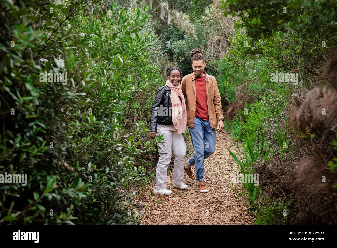 Diverse coppie che camminano braccio in braccio su un sentiero boschivo sotto il cielo coperto su un terreno coperto di foglie Foto Stock