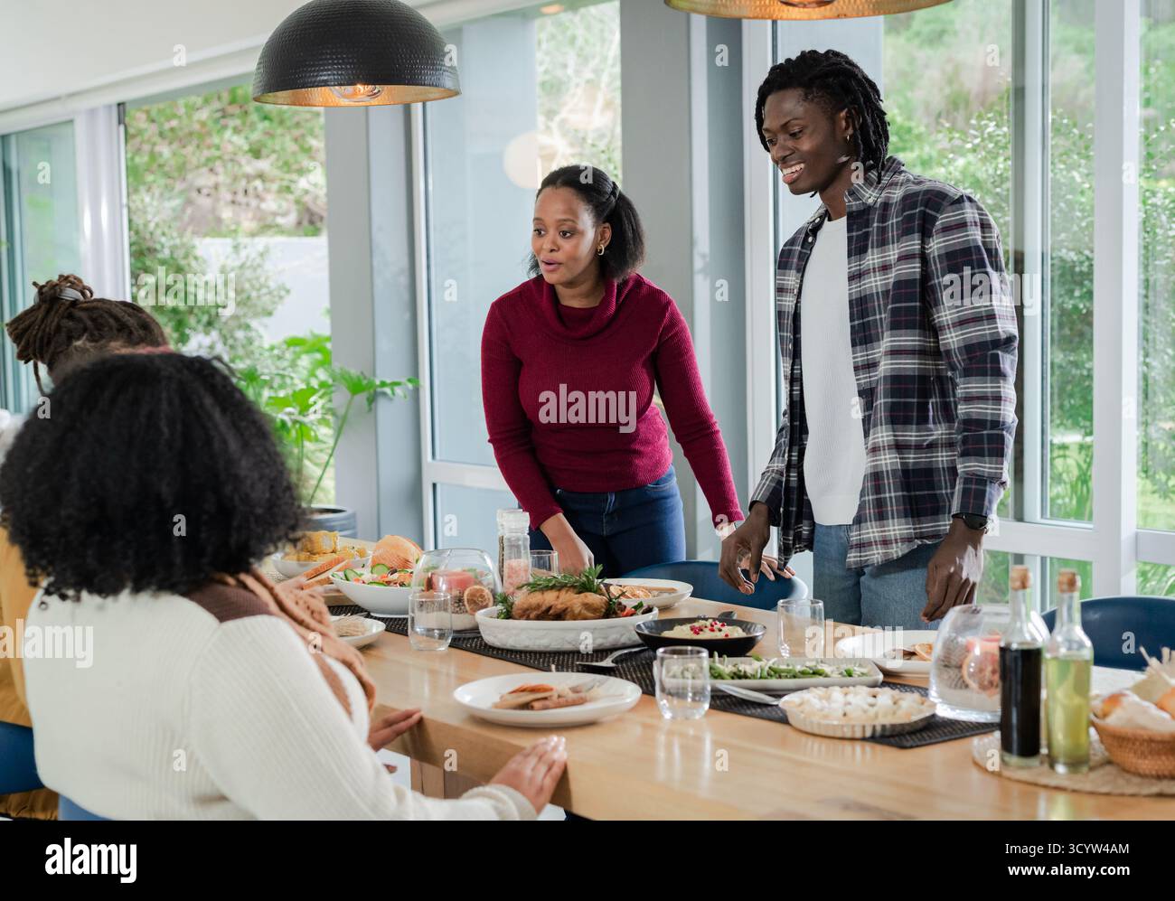 Diversi amici si riuniscono intorno al tavolo di legno a casa con vista sul cortile e servono pollo arrosto e insalata Foto Stock