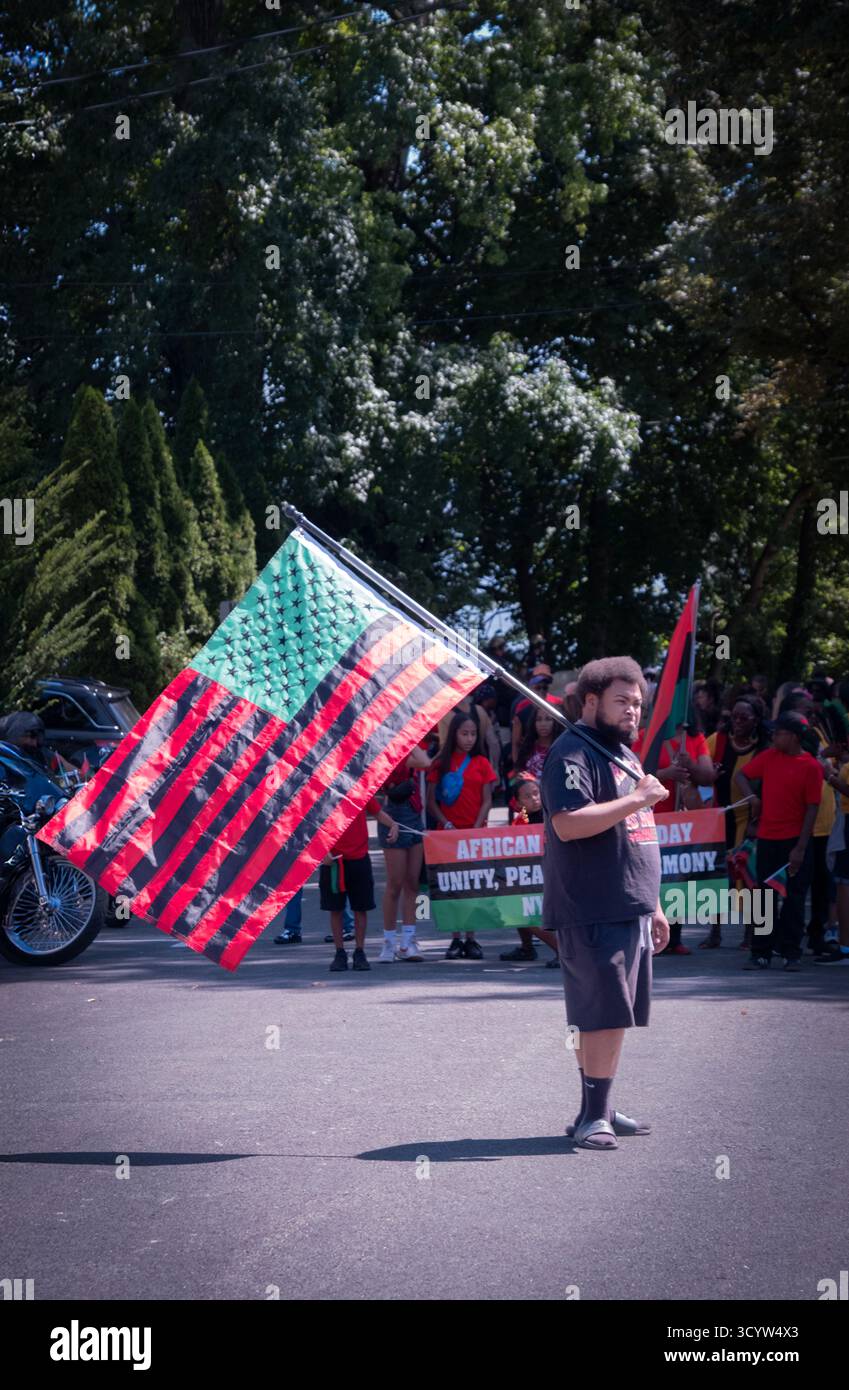 All'inizio della parata afroamericana a Nyack un giovane uomo ha una bandiera americana rossa nera e verde molto grande Foto Stock