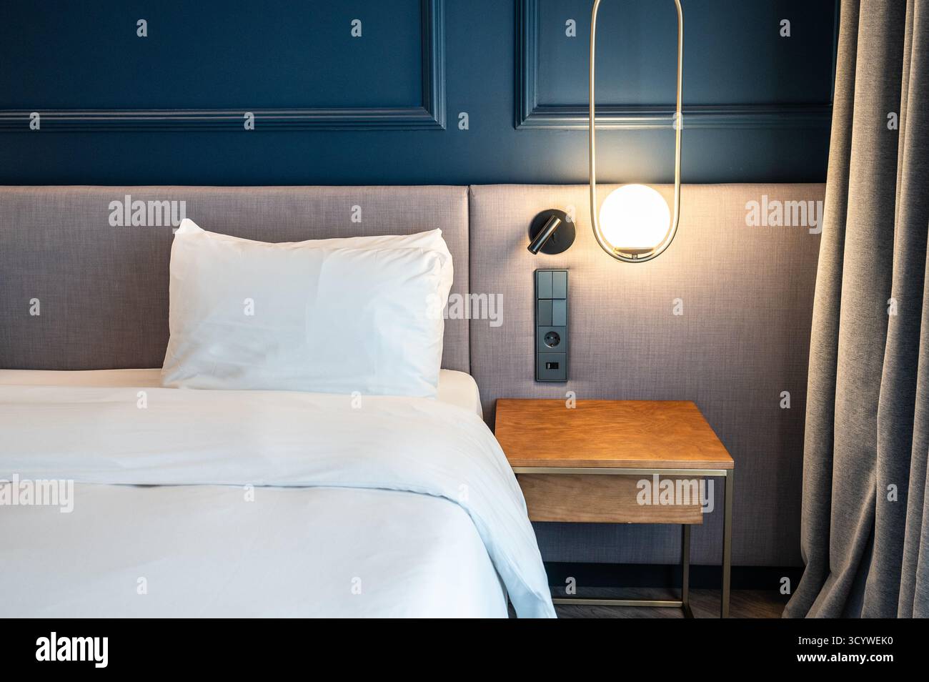 Camera da letto moderna e accogliente con biancheria da letto bianca e illuminazione soffusa Foto Stock