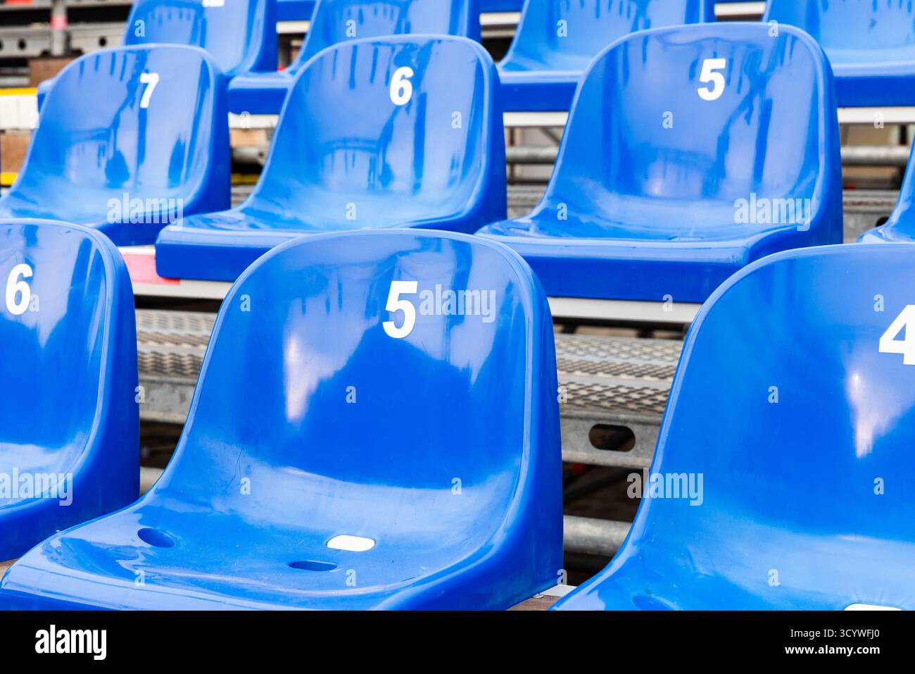 Lo stadio è in plastica blu brillante con 5, 6 e 7 posti a sedere in tribuna vuota, creando un'atmosfera tranquilla e ordinata, perfetta per lo sport, vigilia Foto Stock