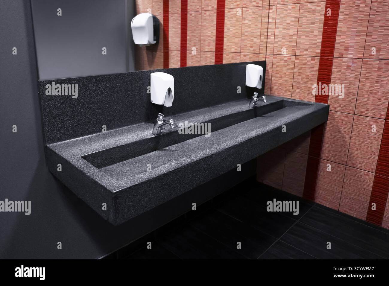 Moderno lavandino in granito per servizi igienici pubblici con acqua calda e fredda, su sfondo piastrellato. Foto di alta qualità Foto Stock