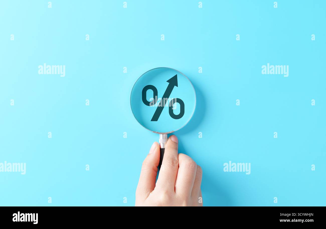 Concetto di crescita del tasso di interesse che mostra una lente d'ingrandimento focalizzata sul simbolo percentuale con freccia rivolta verso l'alto su sfondo blu, che simboleggia la finanza, Foto Stock