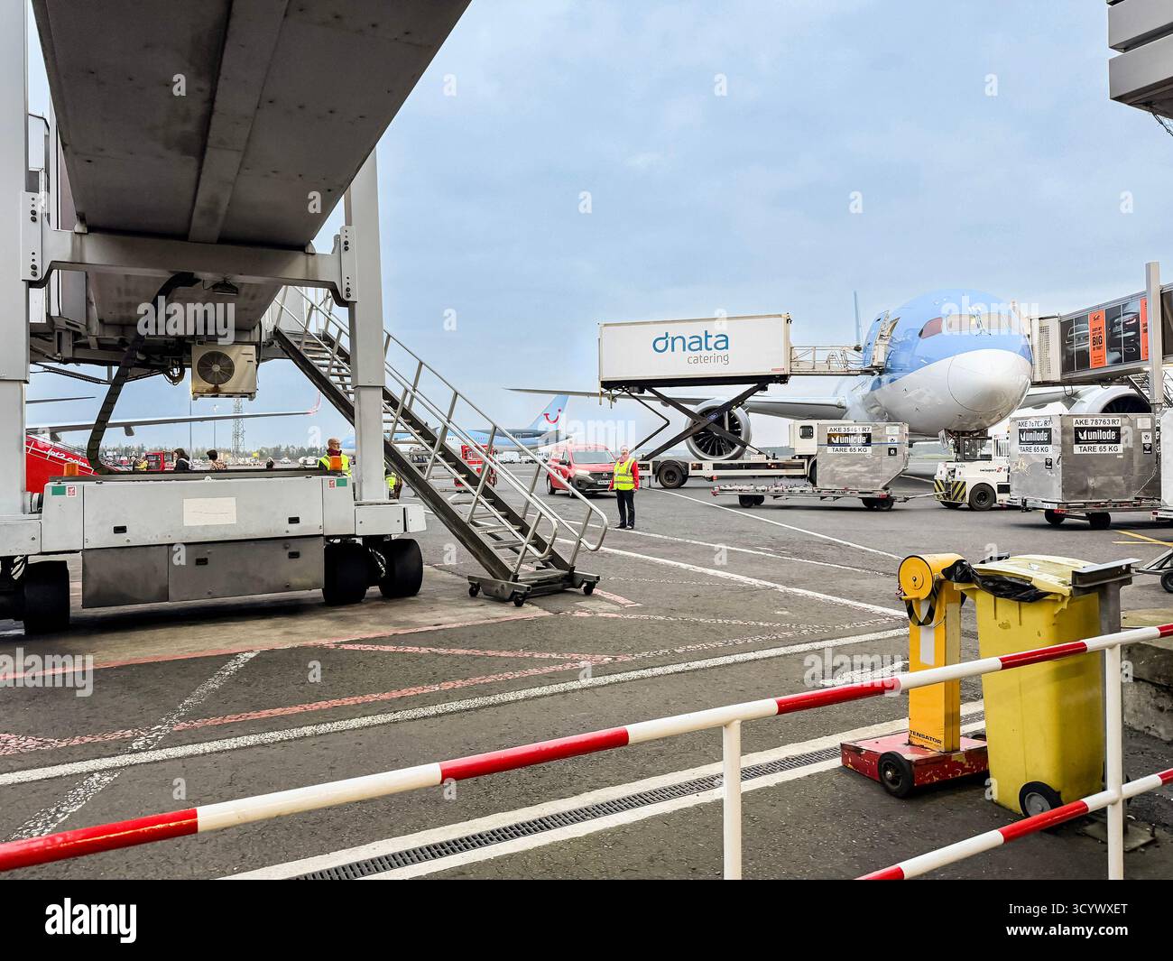 Equipaggio di terra in un aeroporto che prepara un velivolo Tui per la partenza con attrezzature, carrelli e ponte di imbarco passeggeri in vista - Immagine stock catturata con smartphone