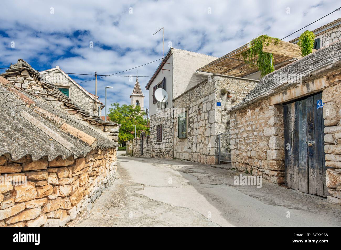 Idilliaco scenario rurale che mostra un affascinante villaggio costruito in pietra con una torre di chiesa circondata dal verde sotto un cielo azzurro. Foto Stock