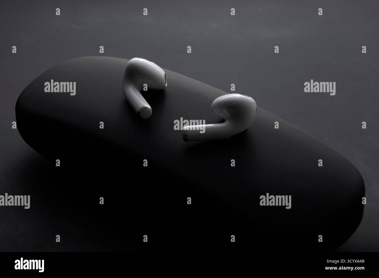 Scatto in studio di auricolari wireless bianchi posizionati su una superficie scura che illustra lo stile di vita minimalista dei dispositivi audio personali e dei moderni dispositivi audio Foto Stock