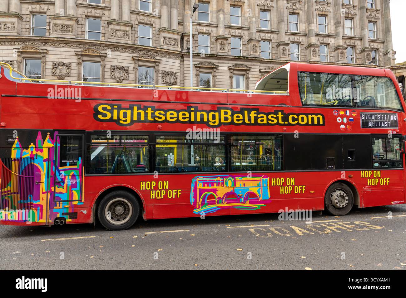 Autobus turistico rosso con grafica colorata parcheggiato in una strada della città di fronte all'architettura storica di Belfast nell'Irlanda del Nord Foto Stock