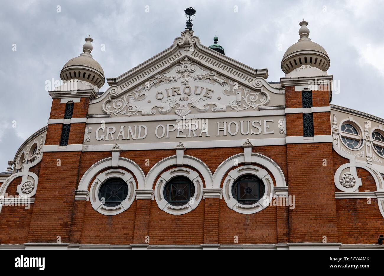 Facciata ornata della Grand Opera House nel centro di Belfast con architettura decorativa e finestre circolari sotto un cielo nuvoloso Foto Stock