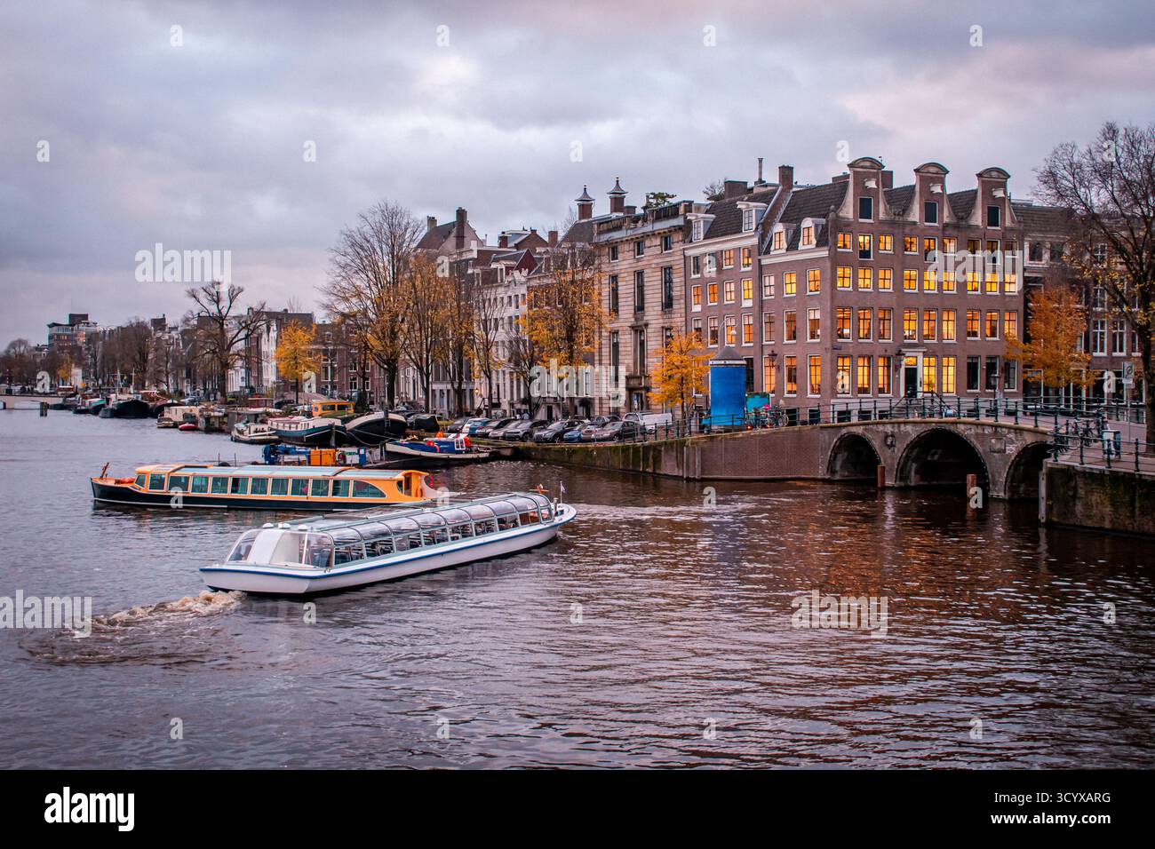 Amsterdam, Paesi Bassi. Il lungomare della città è fiancheggiato da barche ormeggiate, creando una scena affascinante accanto a innumerevoli biciclette ed edifici eleganti Foto Stock