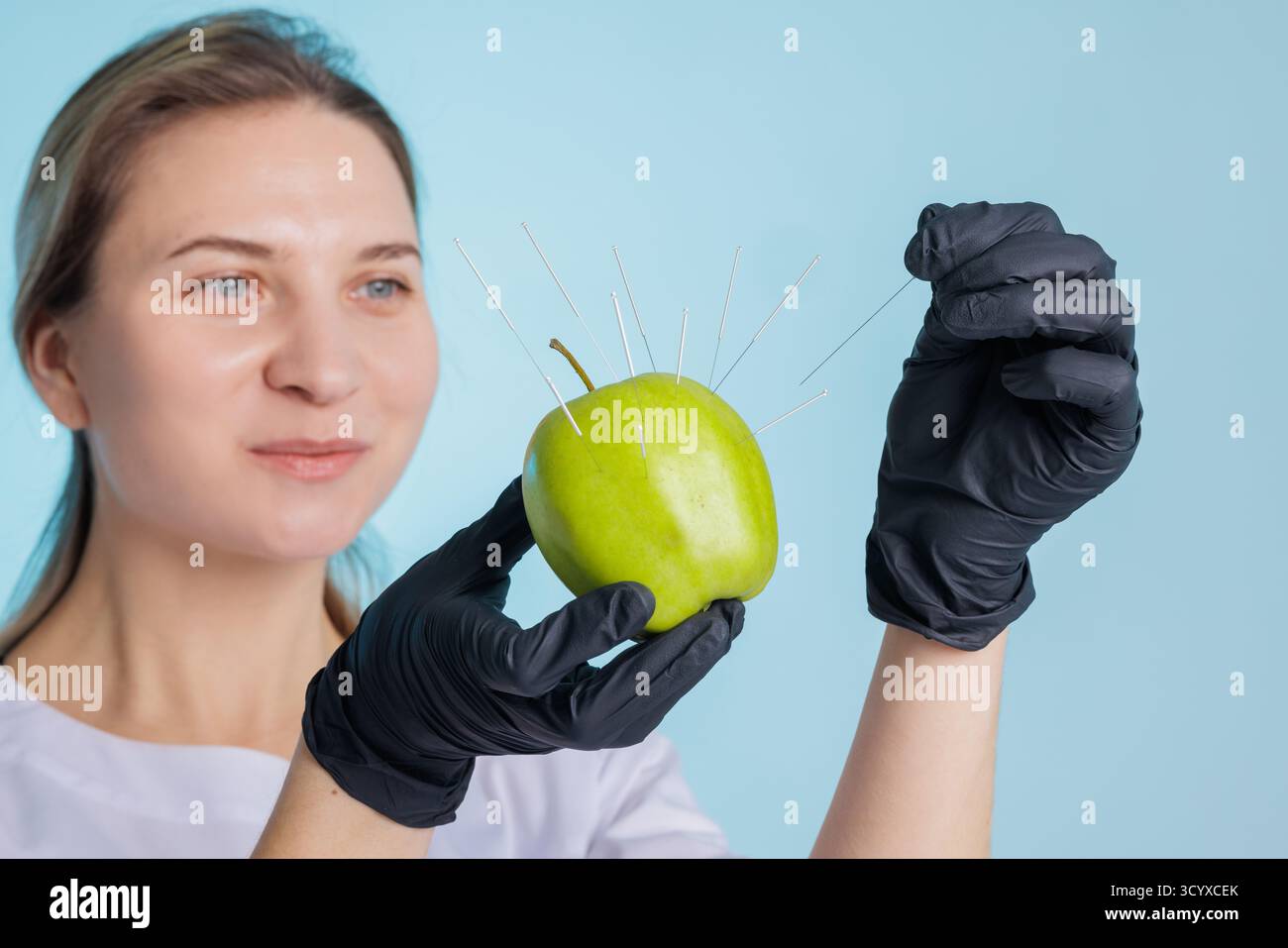 Il terapeuta tiene una mela verde come modello e inserisce aghi sterili per agopuntura, illustrando l'allenamento con aghi asciutti. Foto Stock