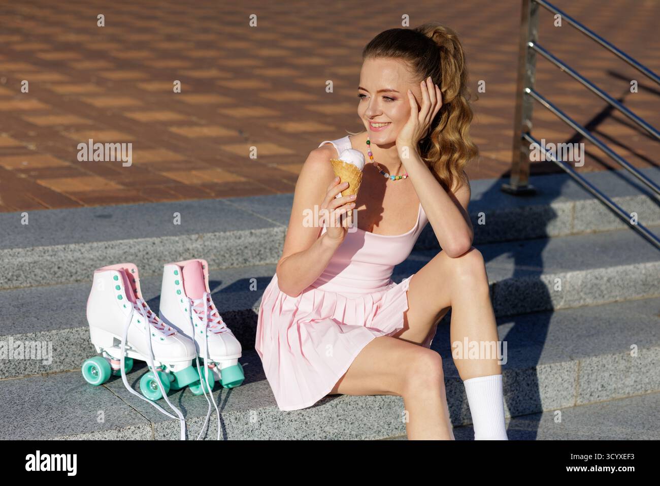 Donna felice seduta sui gradini mangiando gelatina accanto ai pattini retrò, un'estate di sole attività all'aperto Foto Stock