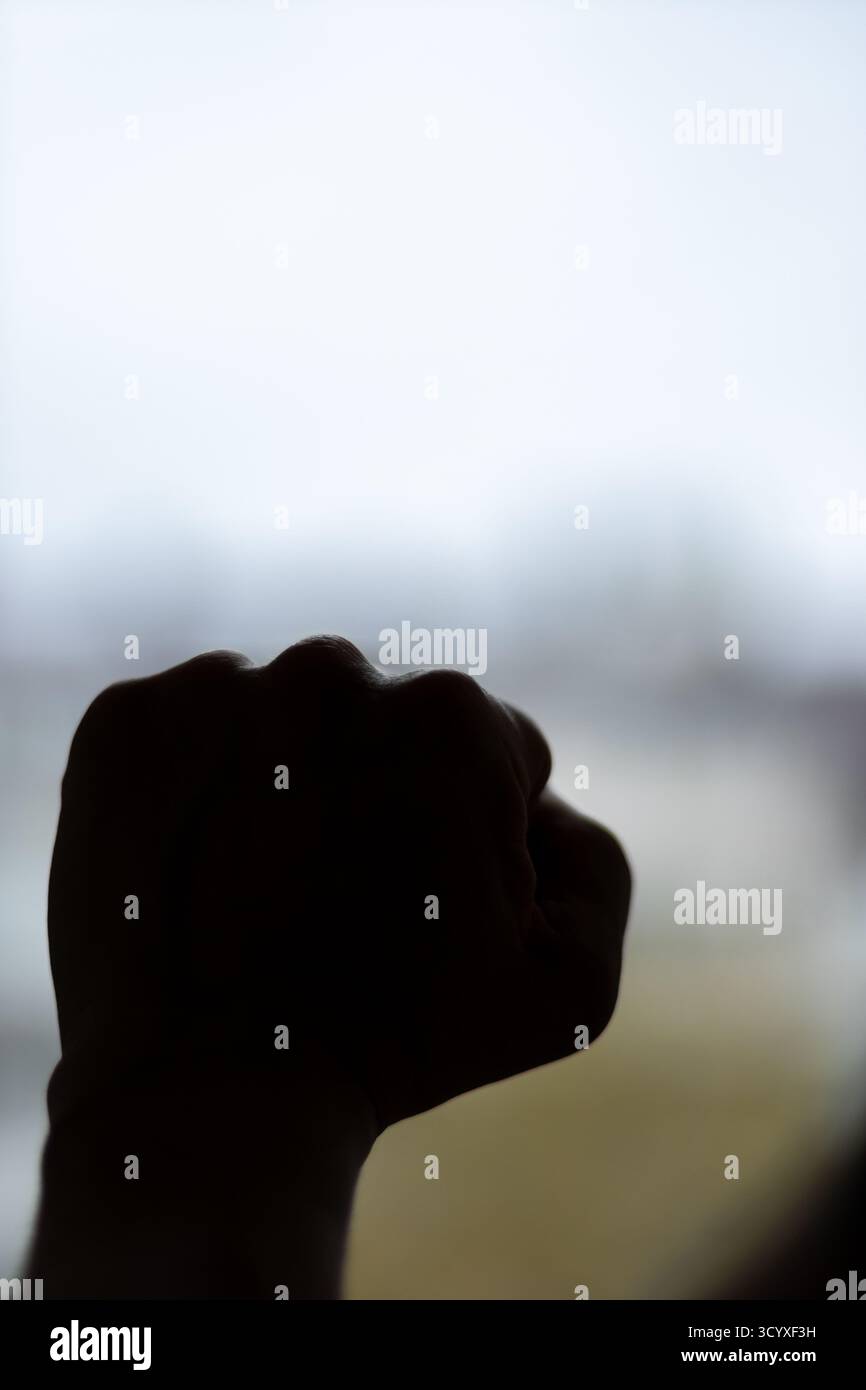 Pugno sagomato in Power Gesture all'aperto. Una forte silhouette retroilluminata di un pugno serrato sollevato contro il cielo, simboleggia determinazione e forza Foto Stock