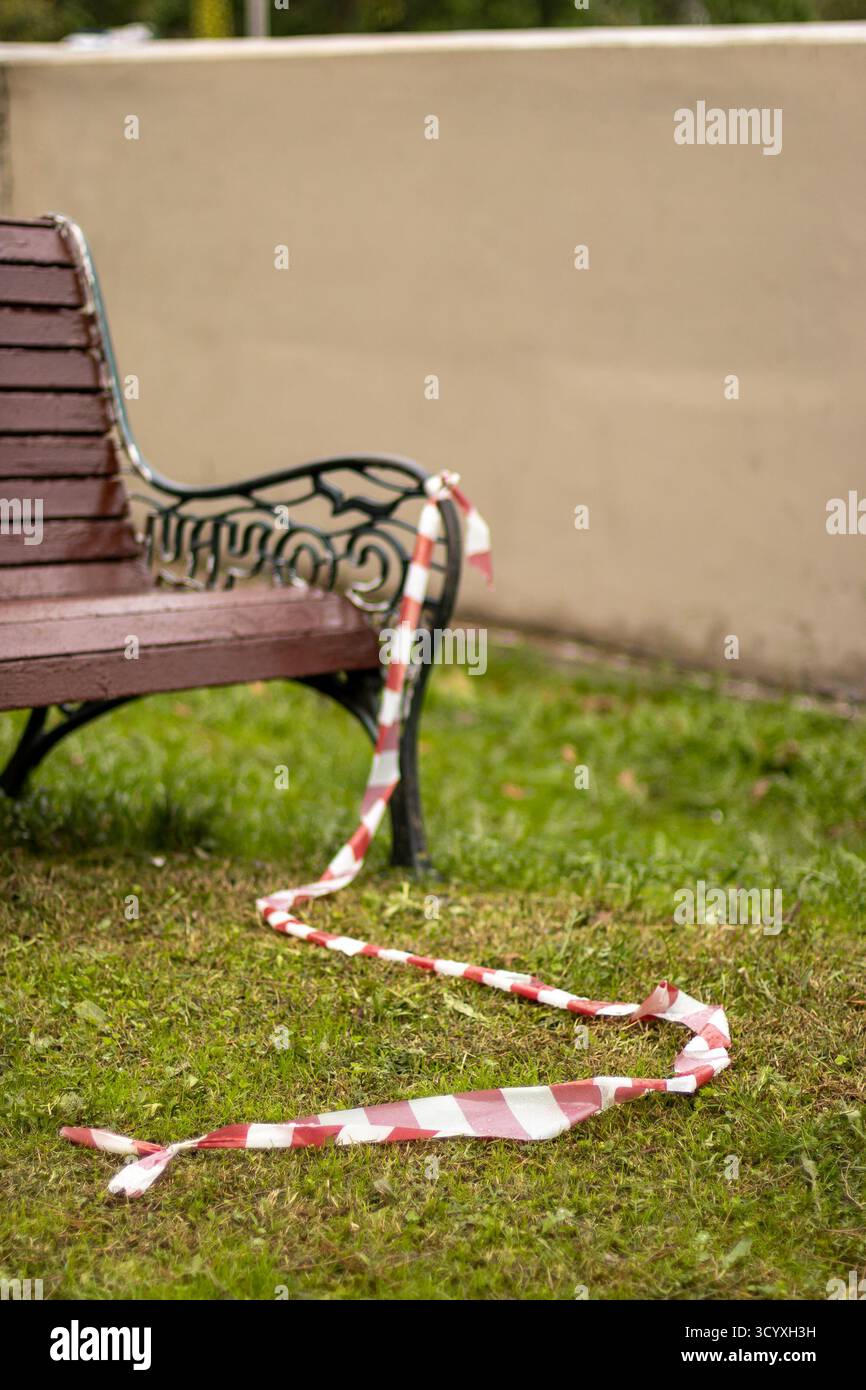 Panca decorata con nastro. Una panchina in legno d'epoca adornata da un lungo nastro a strisce rosse e bianche, adagiata su una parete beige e un gra verde Foto Stock