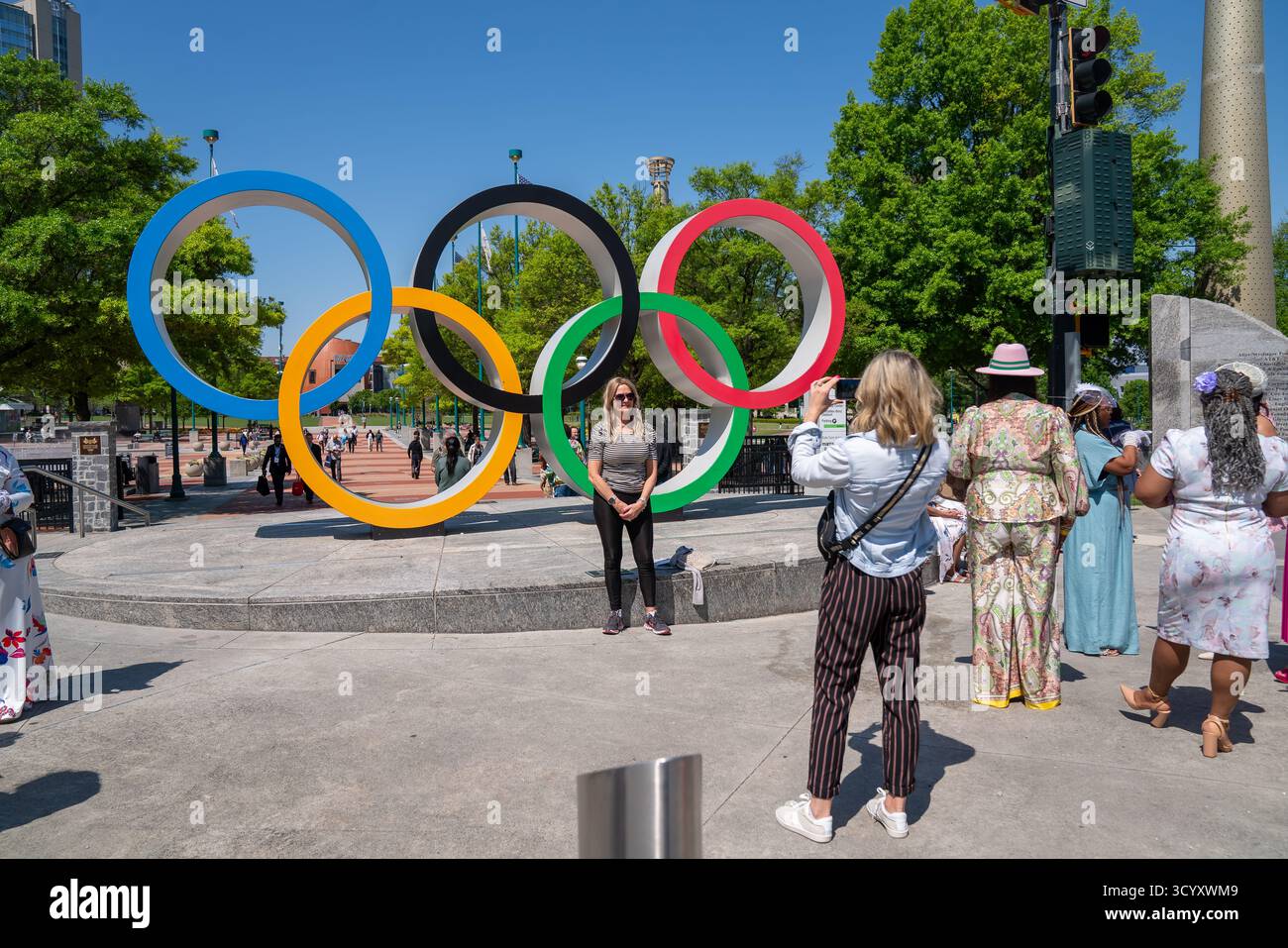 I visitatori posano per le foto di fronte alla scultura degli anelli Olimpici al Centennial Olympic Park in una brillante giornata primaverile, che celebra i Giochi di Atlanta del 1996 Foto Stock