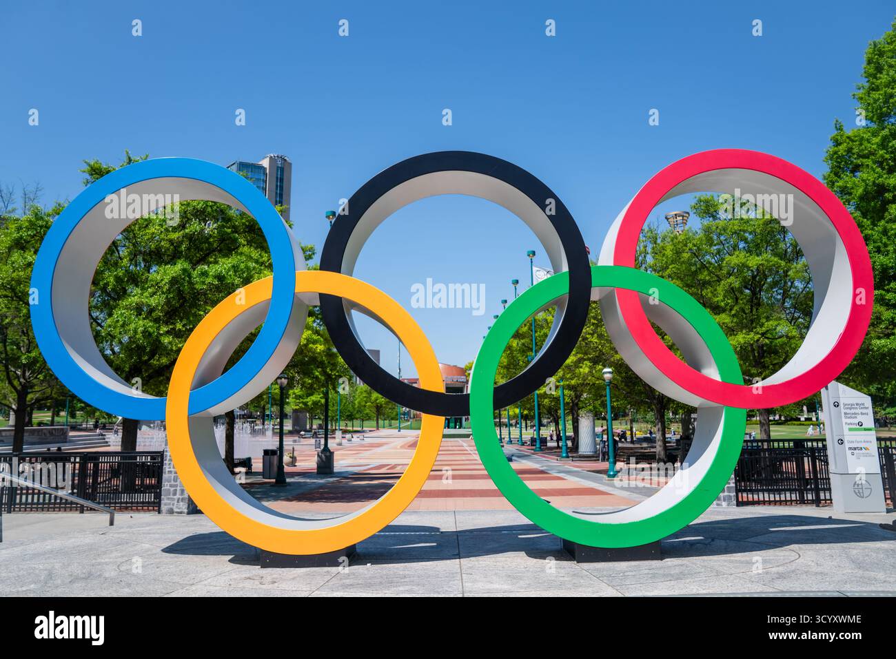 Il colorato monumento degli anelli Olimpici si erge in modo prominente nel Centennial Olympic Park, circondato da alberi e passerelle sotto un cielo primaverile azzurro Foto Stock