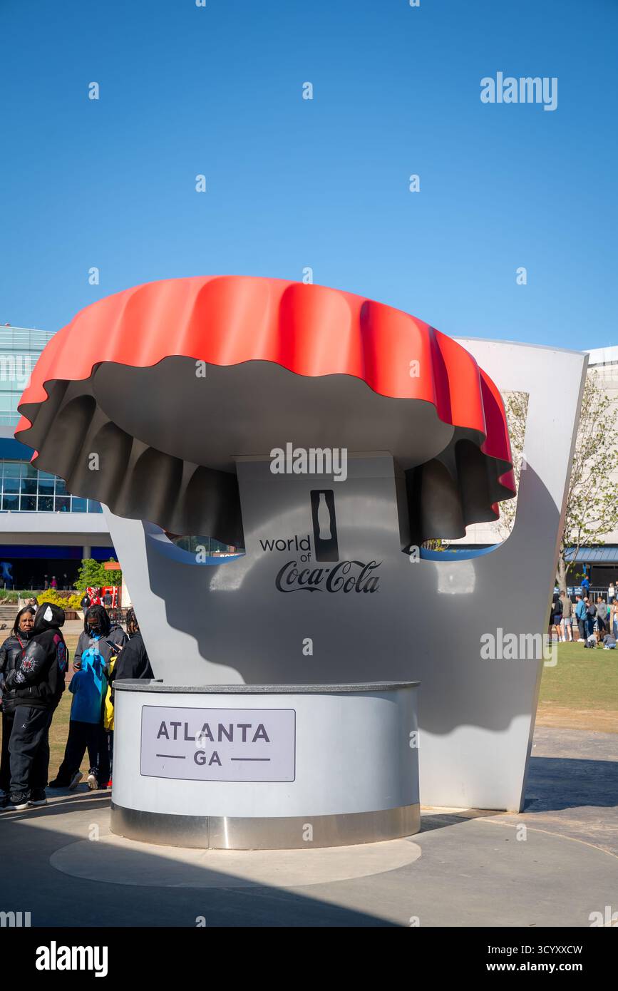 I visitatori si fermano vicino alla grande scultura di berretto rosso all'ingresso del World of Coca-Cola in una mattinata luminosa e soleggiata nel centro di Atlanta Foto Stock