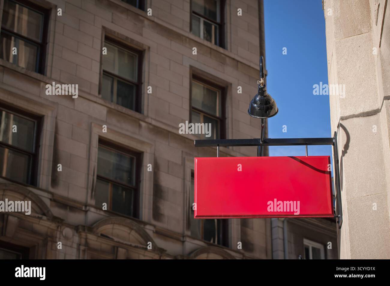 Il cartello rosso vuoto con pensile all'esterno di un negozio cittadino offre spazio per le copie del marchio in un ambiente urbano con una classica facciata in pietra Foto Stock