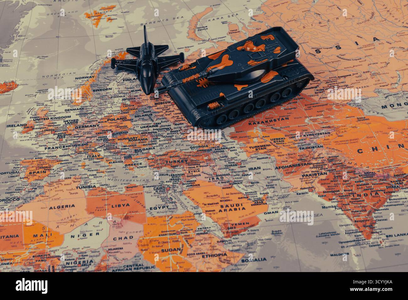 Un serbatoio giocattolo verde e un aereo giocattolo nero sono collocati su una mappa colorata dell'Europa, evidenziando le aree di interesse per la strategia militare nella regione. Foto Stock Un serbatoio giocattolo verde e un aereo giocattolo nero sono collocati su una mappa colorata dell'Europa, evidenziando le aree di interesse per la strategia militare nella regione. Foto Stock