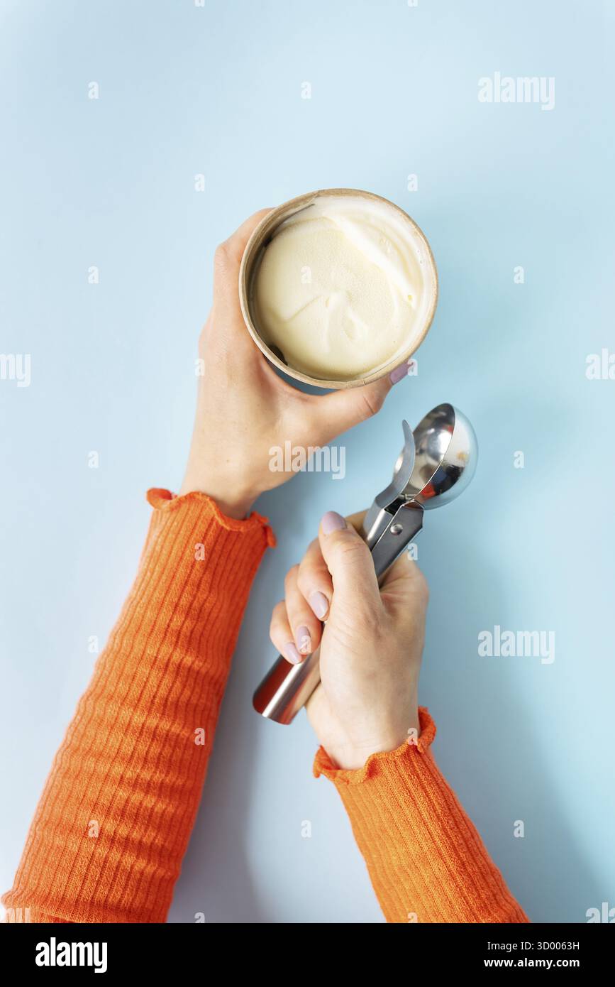 La ragazza tiene in mano un gelato cremoso in un secchio artigianale. Cucchiaio per gelato. Sfondo blu, spazio di copia Foto Stock