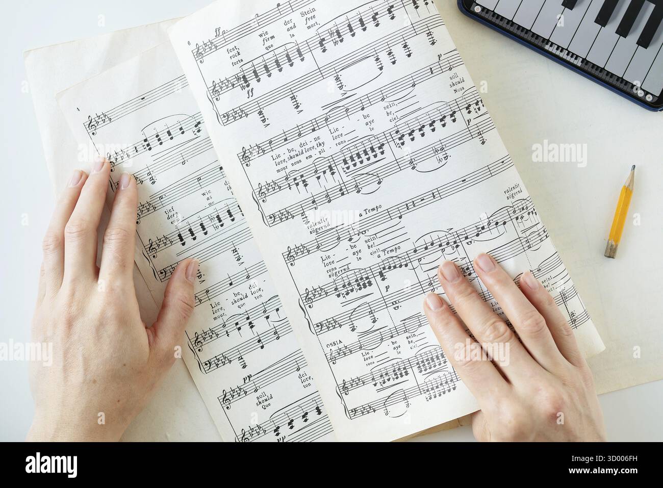 Le mani di una persona vengono viste su uno spartito musicale con una matita e una tastiera sullo sfondo Foto Stock