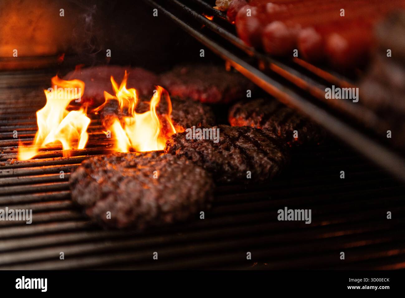 Hamburger cucinati su una grigliata barbecue, hamburger alla griglia con fiamma sul barbecue. West Sussex Regno Unito, estate 2025 Foto Stock