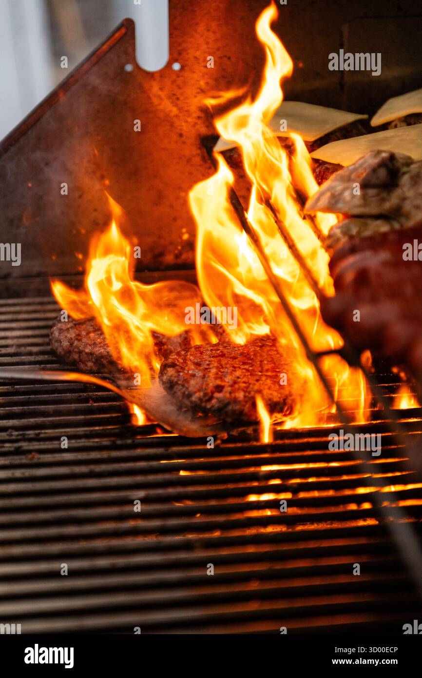 Hamburger cucinati su una grigliata barbecue, hamburger alla griglia con fiamma sul barbecue. West Sussex Regno Unito, estate 2025 Foto Stock