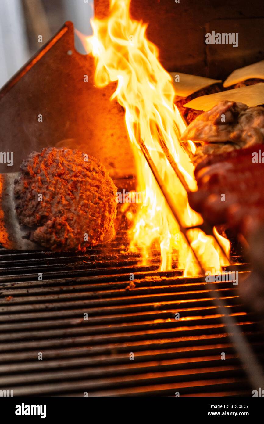 Hamburger cucinati su una grigliata barbecue, hamburger alla griglia con fiamma sul barbecue. West Sussex Regno Unito, estate 2025 Foto Stock