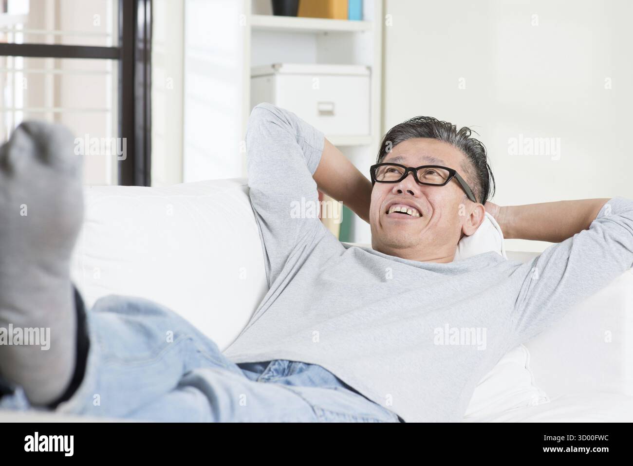 Uomo asiatico maturo anni '50 che sogna ad occhi aperti e riposa a casa. Un uomo cinese anziano rilassato e disteso su un divano interno Foto Stock