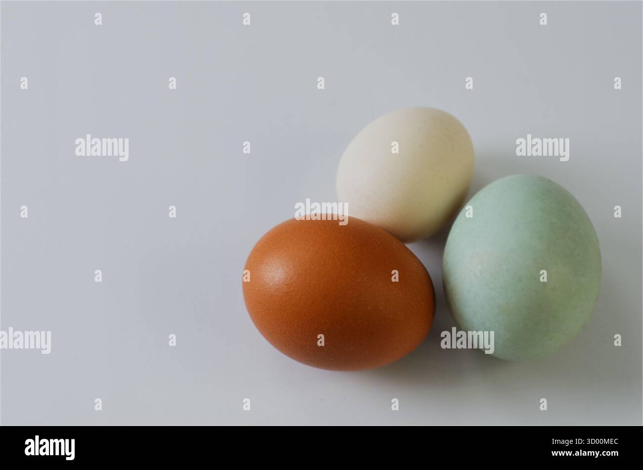 Tre uova colorate su superficie bianca: Uova fresche naturali per cucinare e decorare Foto Stock