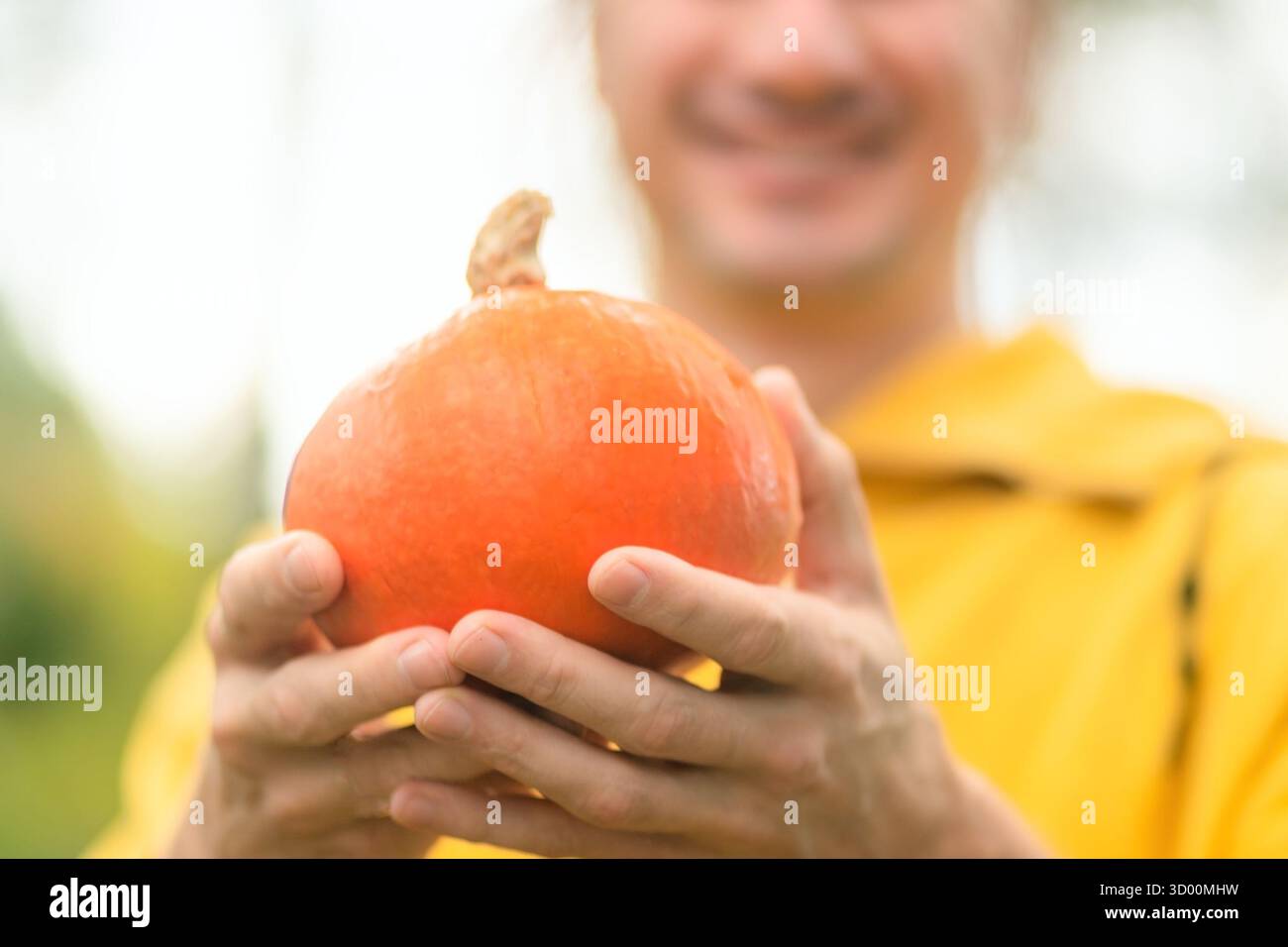 Primo piano di zucca in mani maschili forti, sorridente agricoltore alle spalle. Raccolto autunnale, verdure fresche, alimentazione sana, stile di vita naturale, agricoltura rurale. Foto Stock