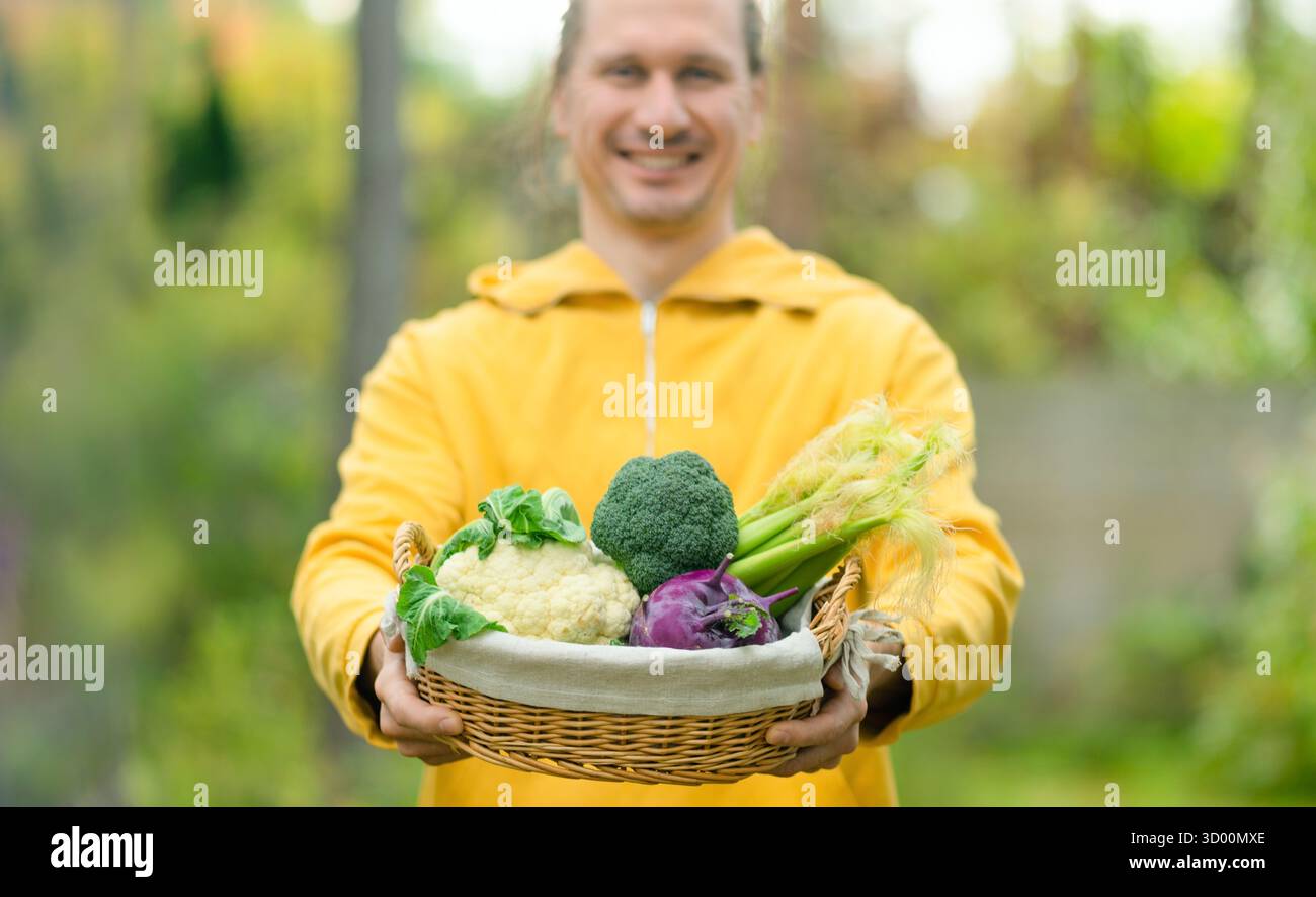 Primo piano di un agricoltore maschio con un cesto pieno di cavolfiore, cavolrabi, broccoli e mais. Verdure fresche, nutrizione sana e orgoglio del raccolto. Foto Stock