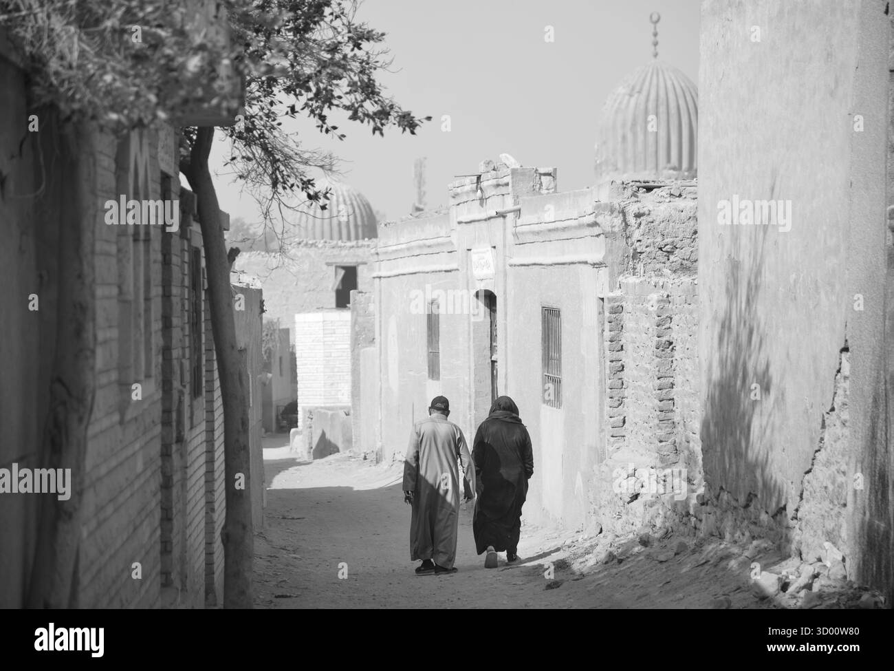 Due persone camminano lungo una strada stretta e polverosa fiancheggiata da vecchi edifici nella città dei morti, il Cairo, in Egitto. Foto Stock