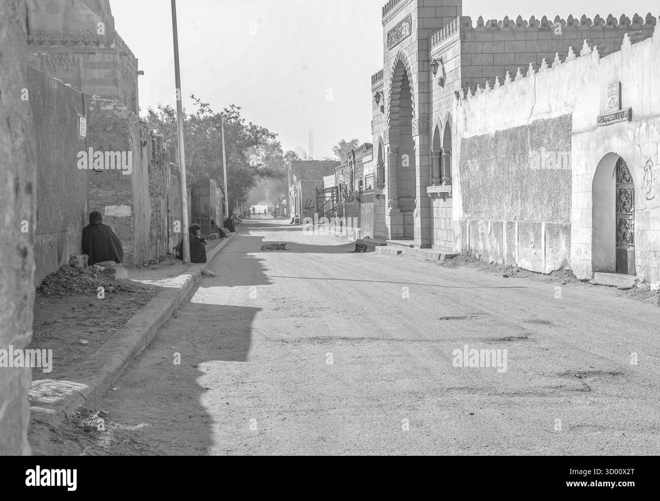 Scena mattutina presso la città dei morti al Cairo, in Egitto, con i residenti seduti lungo una strada tranquilla accanto a mausolei storici e all'architettura delle tombe. Foto Stock