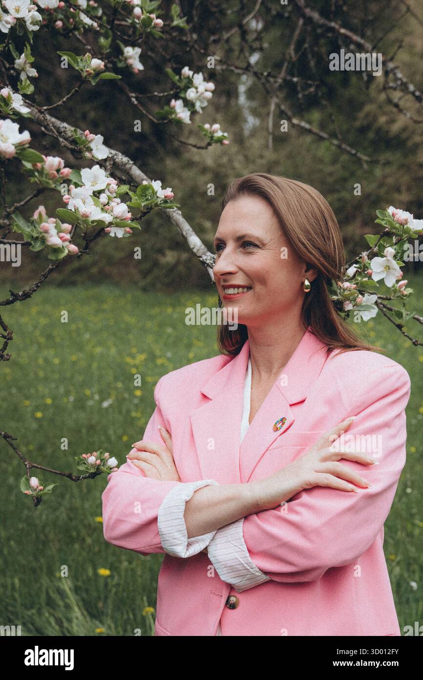 Una donna sorridente di mezza età si trova vicino a un albero in fiore nel giardino primaverile. Bellezza naturale, gioia e armonia con la natura. Rinnovamento stagionale, pace interiore e. Foto Stock