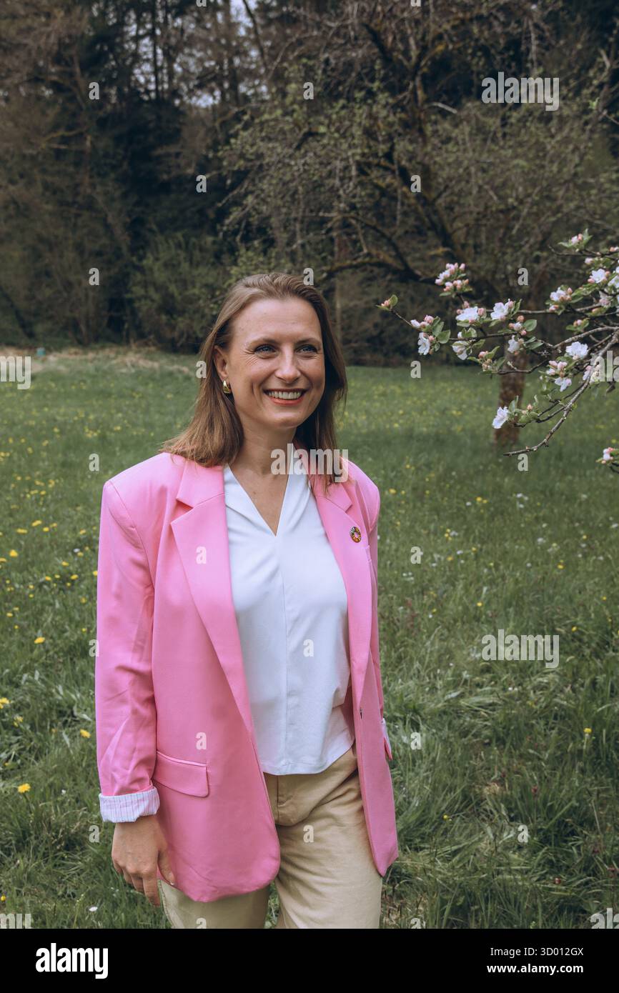 Una donna sorridente di mezza età si trova vicino a un albero in fiore nel giardino primaverile. Bellezza naturale, gioia e armonia con la natura. Rinnovamento stagionale, pace interiore e. Foto Stock