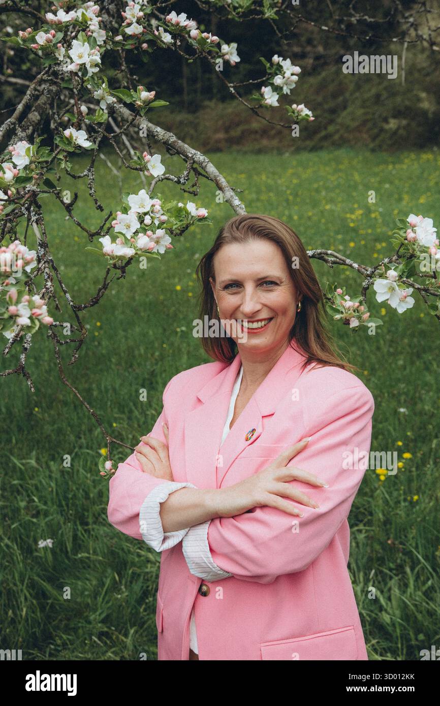 Una donna sorridente di mezza età si trova vicino a un albero in fiore nel giardino primaverile. Bellezza naturale, gioia e armonia con la natura. Rinnovamento stagionale, pace interiore e. Foto Stock