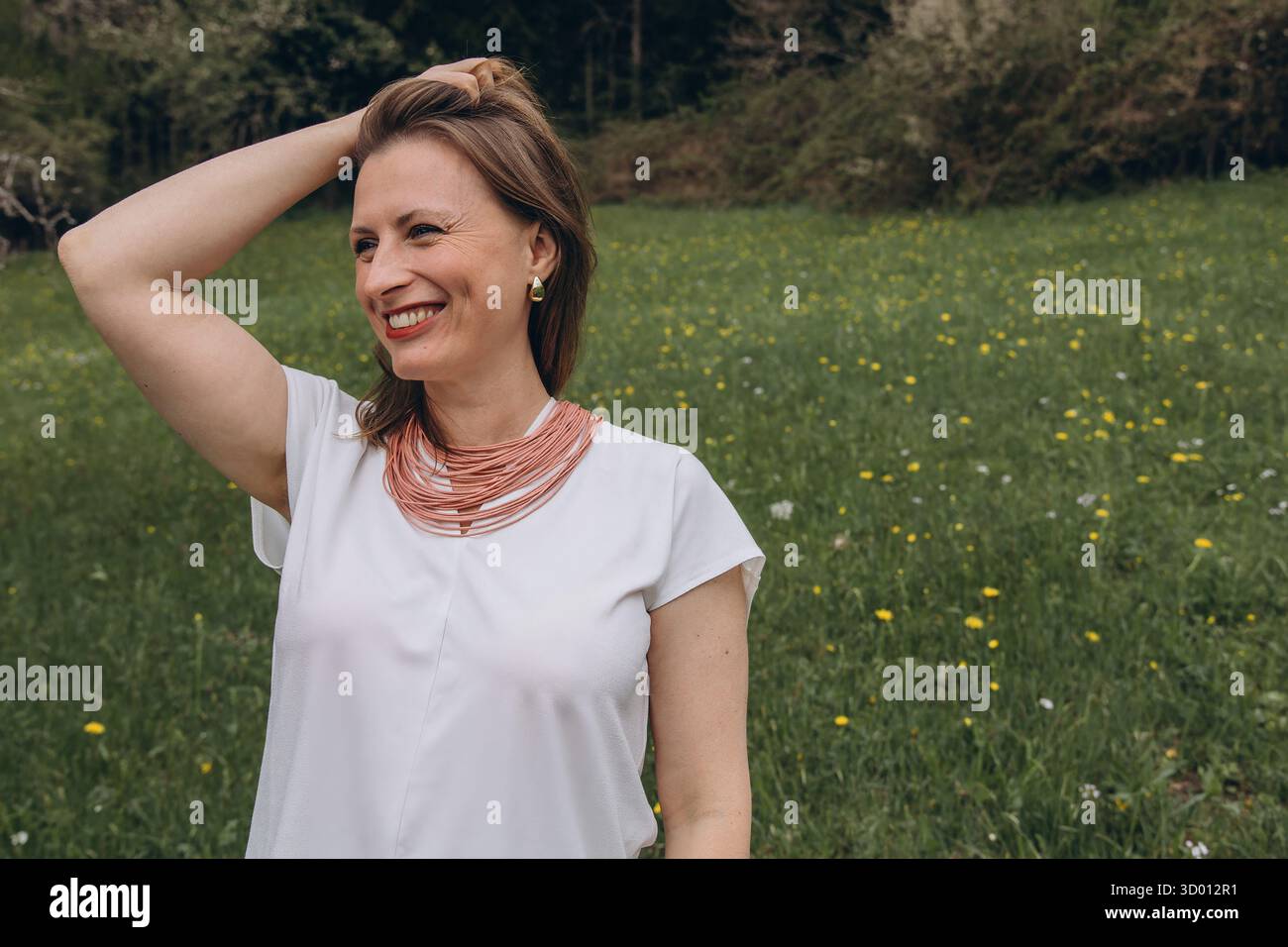 Una donna sorridente di mezza età si trova vicino a un albero in fiore nel giardino primaverile. Bellezza naturale, gioia e armonia con la natura. Rinnovamento stagionale, pace interiore e. Foto Stock