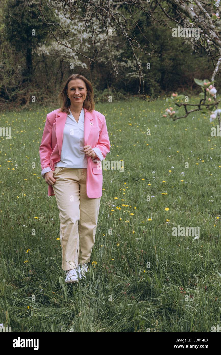 Donna sorridente di mezza età in piedi vicino a un albero in fiore nel giardino primaverile. Concetto di salute femminile, equilibrio ormonale, benessere e bellezza naturale in mi Foto Stock