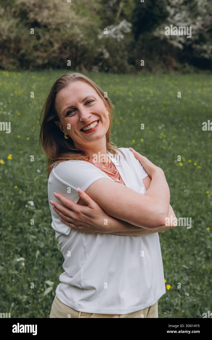 Donna felice di mezza età che ama la natura e si abbraccia nel campo primaverile. Concetto di auto-amore, salute femminile, equilibrio emotivo, consapevolezza, An Foto Stock