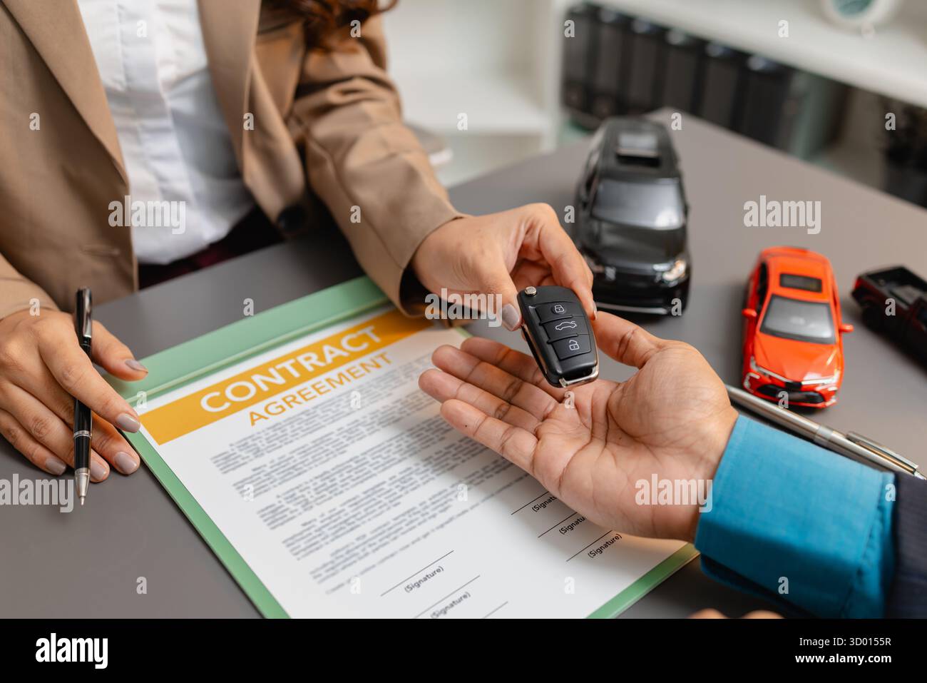 Un uomo d'affari e un cliente stanno esaminando e firmando un contratto di vendita di auto presso una scrivania, con modellini di auto di piccole dimensioni, una tazza di caffè e documenti intorno a loro, Foto Stock