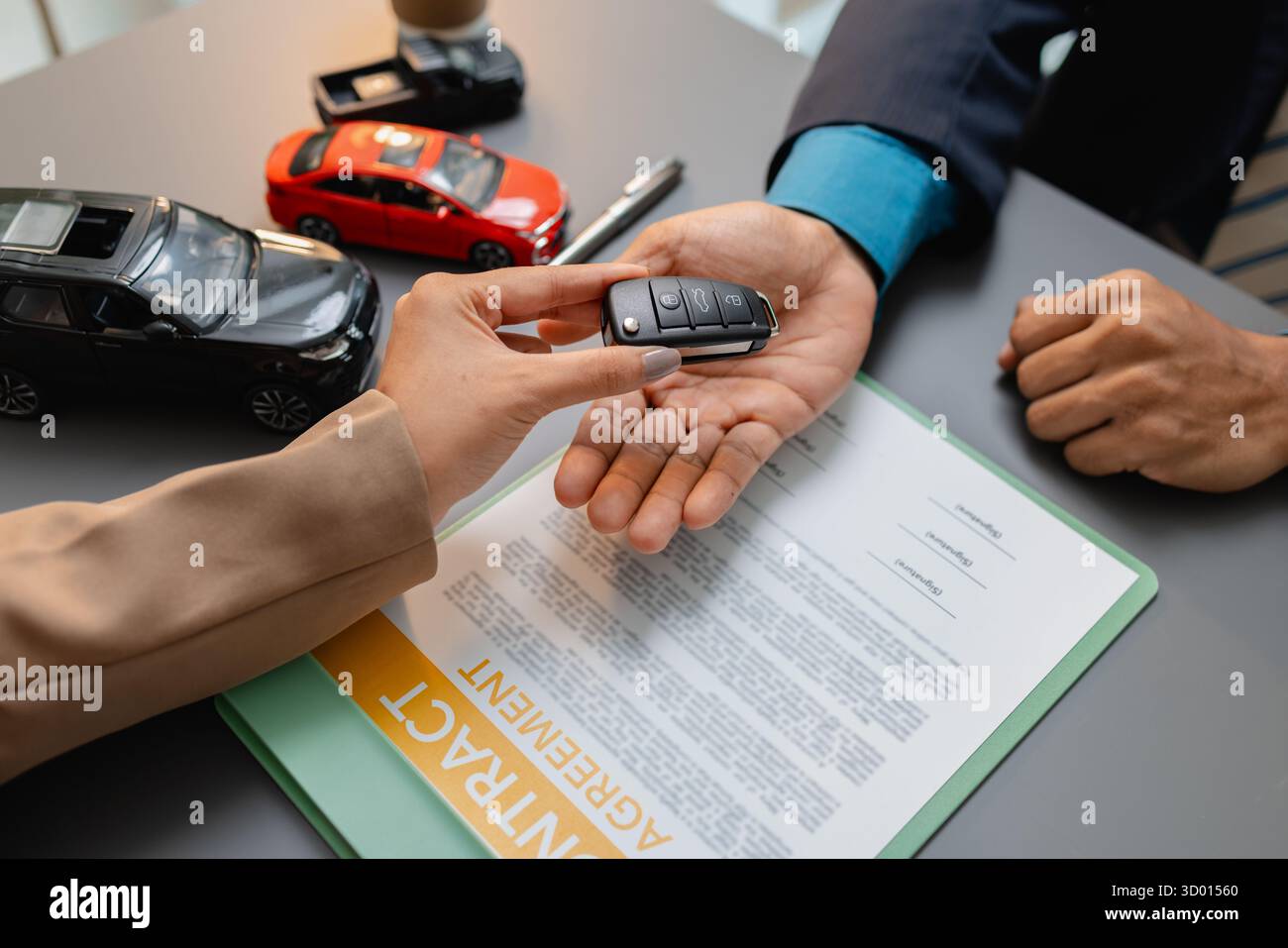 Un uomo d'affari e un cliente stanno esaminando e firmando un contratto di vendita di auto presso una scrivania, con modellini di auto di piccole dimensioni, una tazza di caffè e documenti intorno a loro, Foto Stock