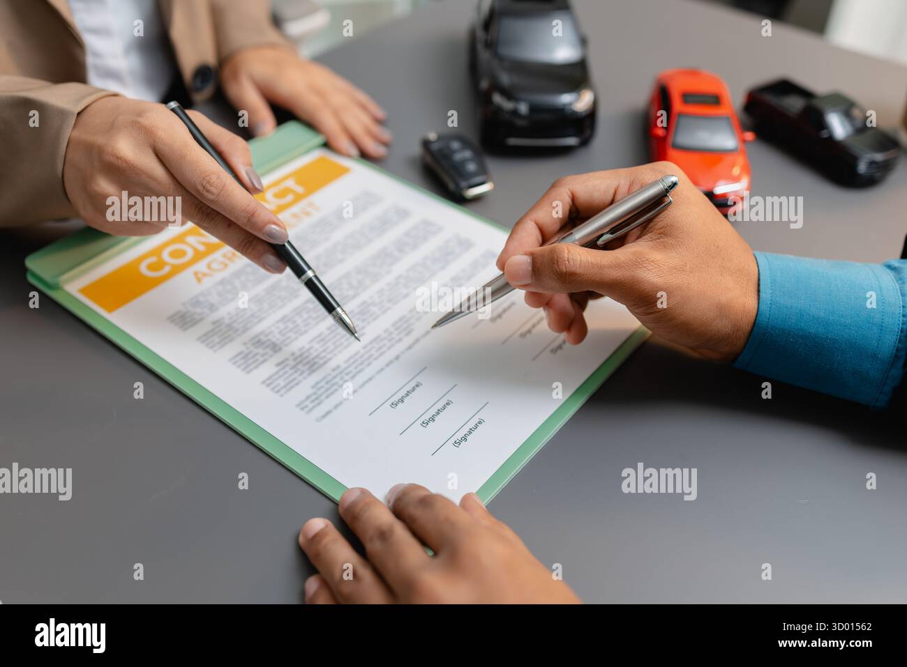 Un uomo d'affari e un cliente stanno esaminando e firmando un contratto di vendita di auto presso una scrivania, con modellini di auto di piccole dimensioni, una tazza di caffè e documenti intorno a loro, Foto Stock