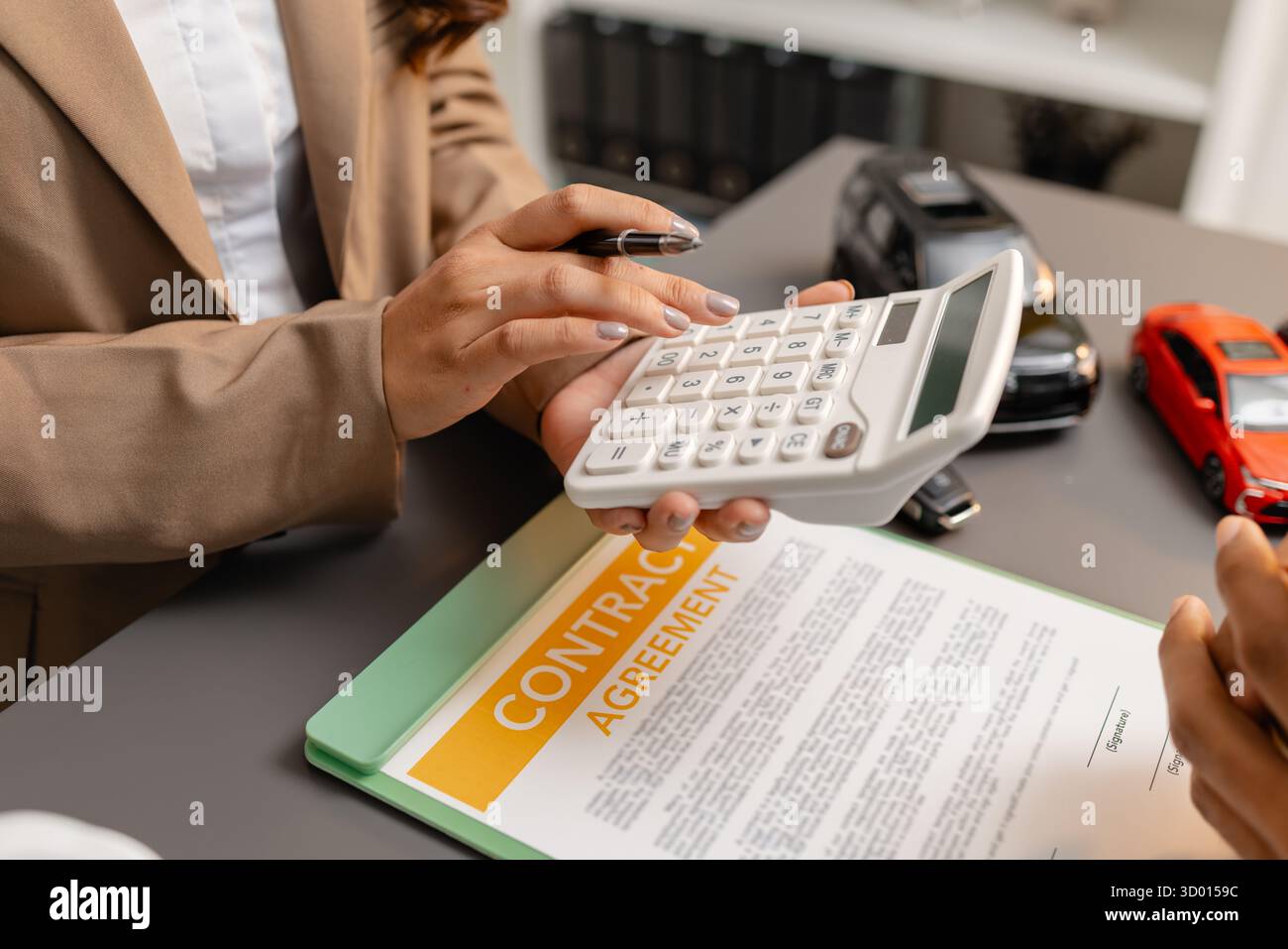 Un uomo d'affari e un cliente stanno esaminando e firmando un contratto di vendita di auto presso una scrivania, con modellini di auto di piccole dimensioni, una tazza di caffè e documenti intorno a loro, Foto Stock
