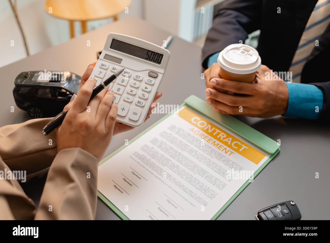 Un uomo d'affari e un cliente stanno esaminando e firmando un contratto di vendita di auto presso una scrivania, con modellini di auto di piccole dimensioni, una tazza di caffè e documenti intorno a loro, Foto Stock