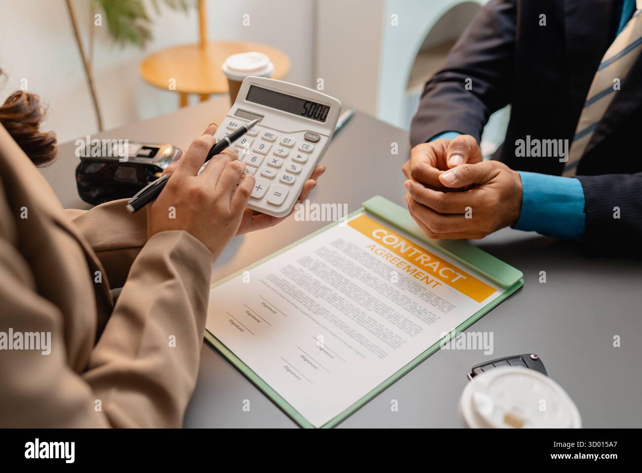 Un uomo d'affari e un cliente stanno esaminando e firmando un contratto di vendita di auto presso una scrivania, con modellini di auto di piccole dimensioni, una tazza di caffè e documenti intorno a loro, Foto Stock