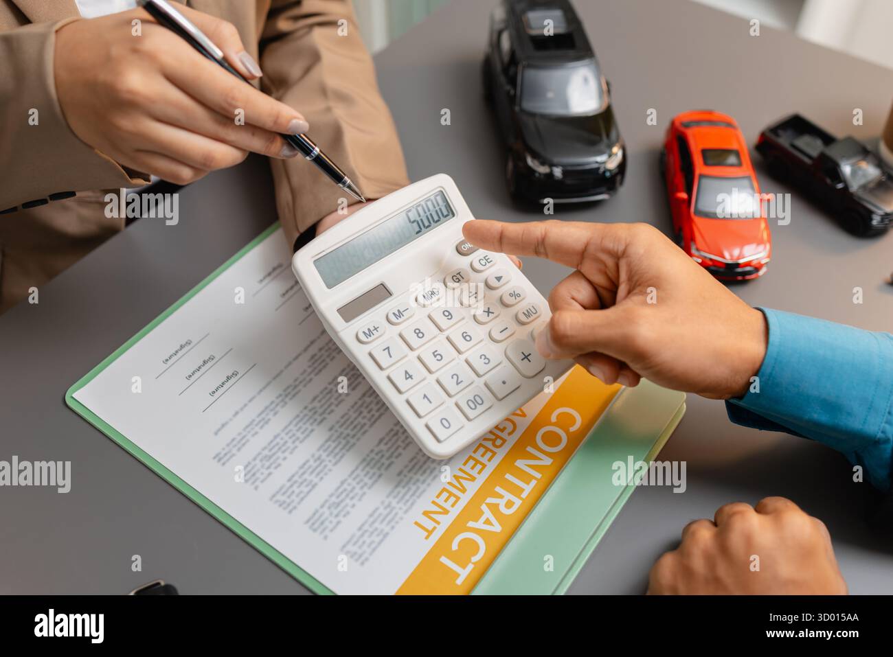 Un uomo d'affari e un cliente stanno esaminando e firmando un contratto di vendita di auto presso una scrivania, con modellini di auto di piccole dimensioni, una tazza di caffè e documenti intorno a loro, Foto Stock